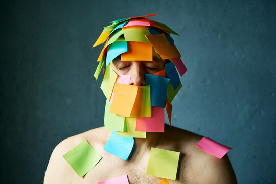 Close up portrait of man with closed eyes and colorful sticky notes all over his face and body over gray background