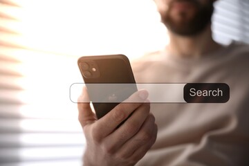 Search bar of website near smartphone. Man using device indoors, closeup