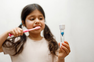 a little girl with dark hair brushes her teeth with a smile, opening her mouth wide, noting the...