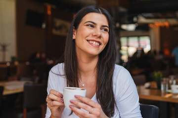 A one young girl or woman is drinking coffee in cafe or restaurant while using her phone to send messages