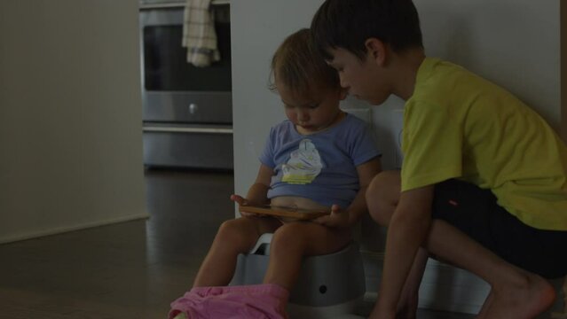 Toddler girl uses the potty watching shows on smart phone as older brother watches