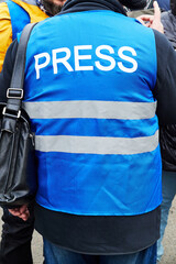 journalist in a blue vest with the inscription press at a rally