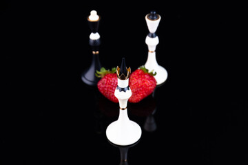 The concept of strategy, choice, association, merger, victory. Chess pieces and strawberries on a black background. Selective focus.
