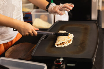 Obraz na płótnie Canvas Woman preparing fresh quesadilla on black grill at local food market.