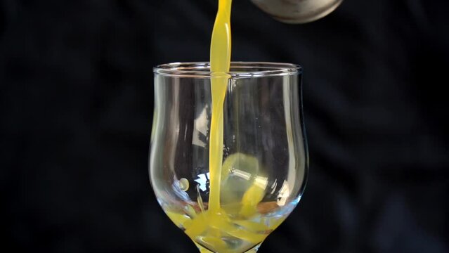 Fresh mango juice pours into a glass against a black background. Pouring orange juice stream from jug into glass with blurred black background. slow motion