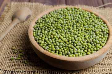 Green mung beans in a bowl on burlap on a wooden table. Organic legumes. Vegan and vegetarian food. Rustic style. The concept of healthy eating. Horizontal orientation. Selective focus.