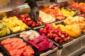 a person wearing a glove is cutting up fruit in a display case.