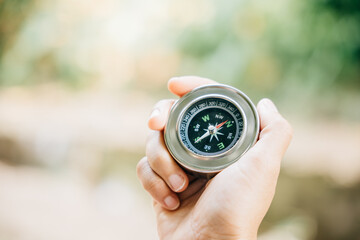 A traveler holding a compass in a park seeking guidance and direction. The compass in the woman hand against a nature-blurred background signifies exploration and a journey to find one way.