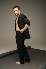 fashionable and handsome man with bare chest and pinstripe suit posing on grey background