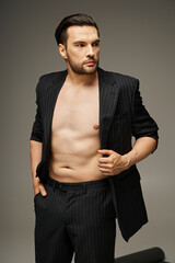 fashion statement concept, daring and shirtless man in pinstripe suit posing on grey background