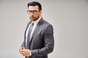 handsome businessman in formal wear and glasses standing on grey background, elegance and style