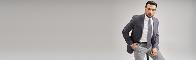 handsome businessman in formal wear posing with hand in pocket and sitting on high stool, banner