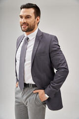 portrait of cheerful businessman in stylish attire posing with hands in pockets on grey background