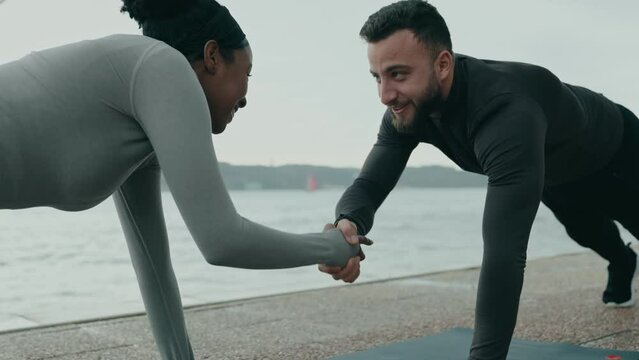 Fitness duo showcases teamwork, strength, and fun in an outdoor plank exercise, emphasizing the dynamic interaction between a Middle Eastern man and an African woman