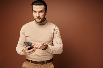 good looking man with bristle in turtleneck using his smartphone on beige background, social media
