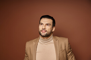 Obraz premium dreamy and handsome man with bristle smiling and posing in stylish beige blazer on beige backdrop