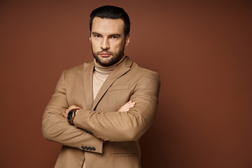 handsome man in turtleneck and blazer giving confident look while standing with folded arms on beige