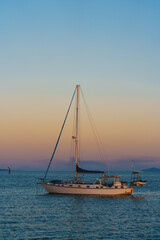 Fototapeta premium A sailboat is floating on the ocean with a beautiful sunset in the background
