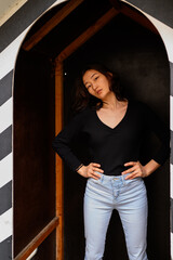 A young woman in a chic black top and light blue jeans poses in a unique architectural doorway with a black and white checkered pattern.