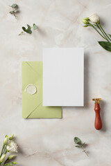Wedding invitation mockup and olive envelope on stone background with flowers. Elegant wedding flat lay composition. Top view.