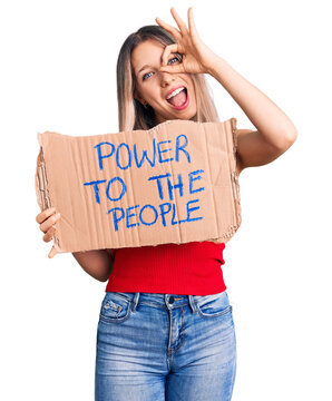 Young beautiful blonde woman holding power to the people banner smiling happy doing ok sign with hand on eye looking through fingers
