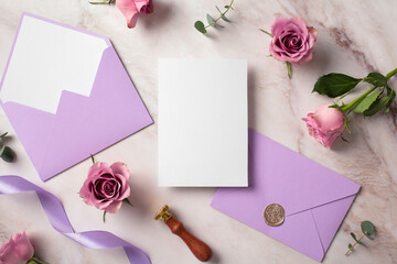 Wedding invitation card template. Top view photo of blank paper card, purple envelopes, ribbon, rose flowers on marble background.