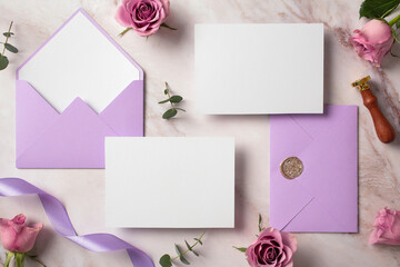 Wedding stationery kit. Purple envelope and blank invitation cards on marble background with ribbon and roses flowers. Elegant wedding flat lay composition.