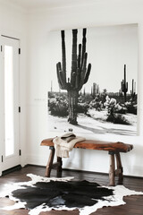 A black and white photograph of cacti in the desert on a wall above a wood bench. A modern home entryway with a cowhide rug, symmetrical white walls, and high contrast,in style of modern home entryway