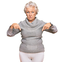 Senior grey-haired woman wearing casual winter sweater pointing down looking sad and upset,...