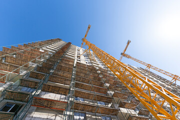Construction of a multi-storey building using a high-rise yellow crane. Home construction. Crane and building under construction against blue sky. Construction work site.