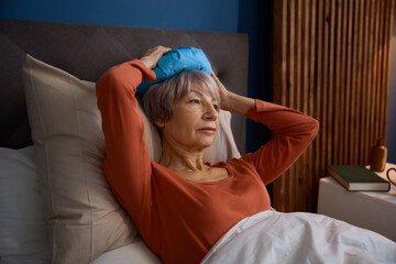 Senior woman with headache feeling upset unhappy lying in bed - obrazy, fototapety, plakaty