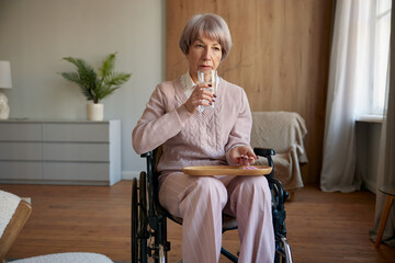 Lonely sad old woman in wheelchair taking prescribed pills at hospice - obrazy, fototapety, plakaty