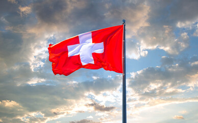 Flag of Switzerland flying in the wind against a cloudy sky.