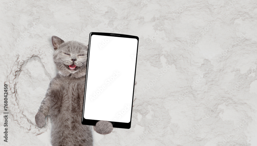 Poster Happy cat making snow angel while lying on snow and holding smartphone with white blank screen in it paw. Empty space for text