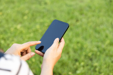 Close-up hand holding touch smart phone on nature background. Woman using mobile phone in the city park