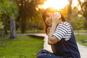 Beautiful woman smile in headphones listening to the music while sitting in the park. Enjoying her...