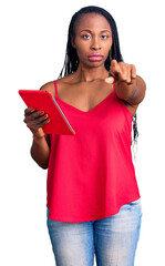 Young african american woman holding touchpad pointing with finger to the camera and to you, confident gesture looking serious