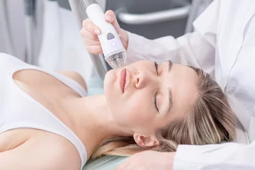 Tuinposter Pretty young woman client lying with closed eyes and getting stimulating beauty facial treatment during rf-lifting and vacuum massage procedure at clinic. Radiofrequency face lifting © Ermolaev Alexandr