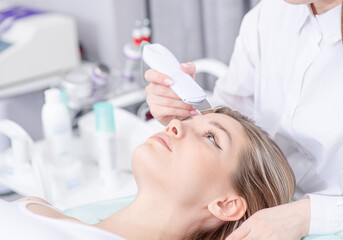 Beautiful woman receiving ultrasound cavitation facial peeling at spa salon. Cosmetology and facial skin care. Profissional facial treatment and face cleansing - 768045665