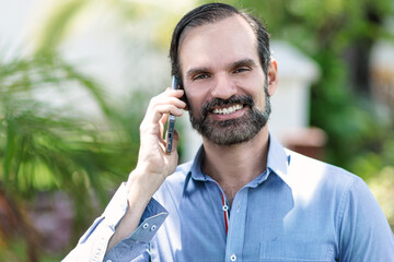Elegante hombre adulto ejecutivo latino sonriente hablando por teléfono en parque, zona urbana