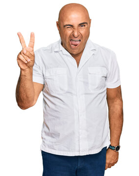 Mature middle east man with mustache wearing casual white shirt smiling with happy face winking at the camera doing victory sign with fingers. number two.