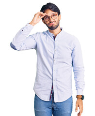 Fototapeta premium Handsome hispanic man wearing business shirt and glasses worried and stressed about a problem with hand on forehead, nervous and anxious for crisis
