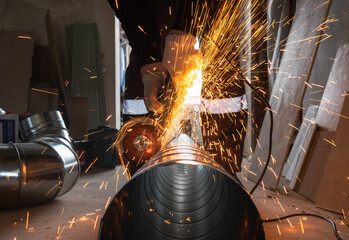 a worker cuts a ventilation pipe with an angle grinder