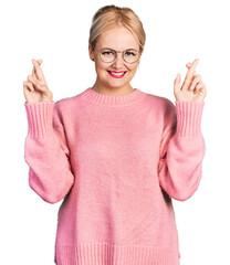 Young blonde woman wearing casual clothes and glasses gesturing finger crossed smiling with hope and eyes closed. luck and superstitious concept.