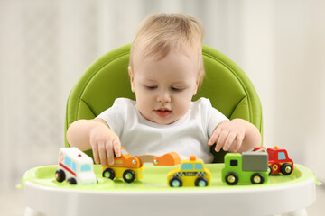 Children toys. Cute little boy playing with toy cars in high chair at home