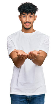 Young arab man wearing casual white t shirt smiling with hands palms together receiving or giving gesture. hold and protection