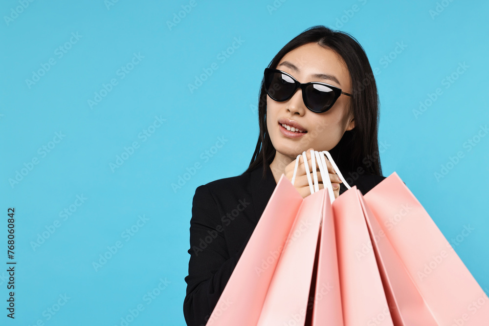 Sticker Smiling woman with shopping bags on light blue background. Space for text