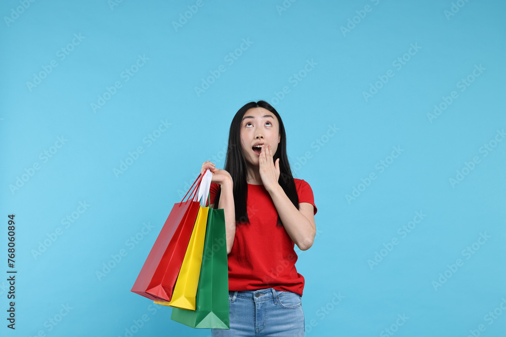 Canvas Prints Surprised woman with shopping bags on light blue background