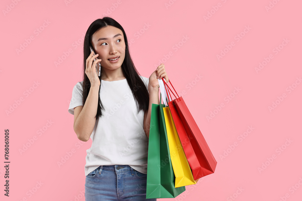 Sticker Smiling woman with shopping bags talking by smartphone on pink background. Space for text