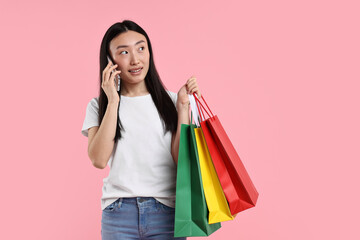 Smiling woman with shopping bags talking by smartphone on pink background. Space for text